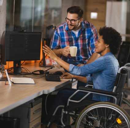 Disabled computer programmer sitting in a wheelchair at workplace and collaborating with a colleague